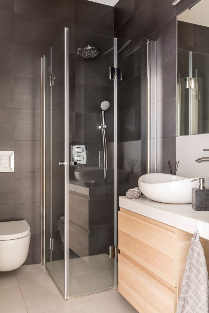 Corner shower with dark tile and a wood floating vanity