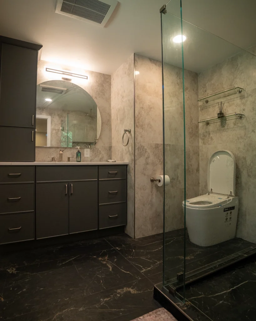 Bathroom remodel with frameless glass shower, gray vanity and black marble floor