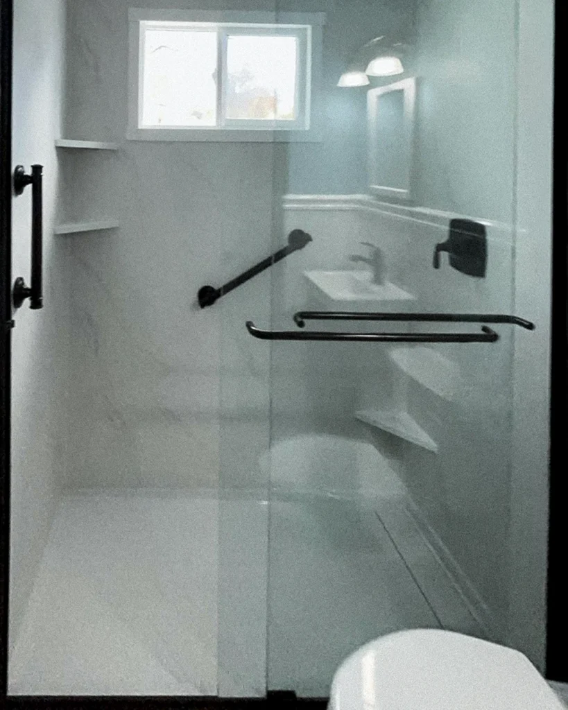 Walk-in shower with glass door, grab bar and corner shelves
