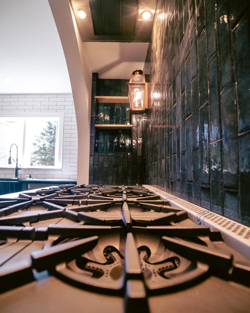 Professional gas range under an arched dark tile wall