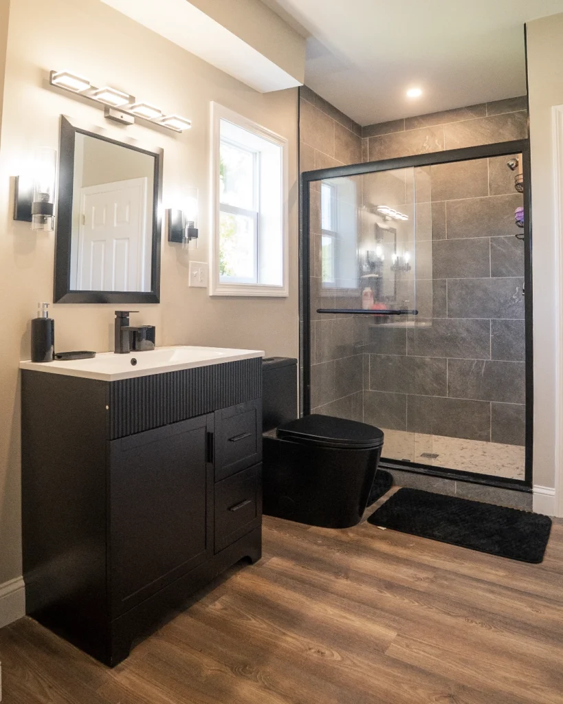 Bathroom remodel with black vanity, framed glass shower and wood-look floor